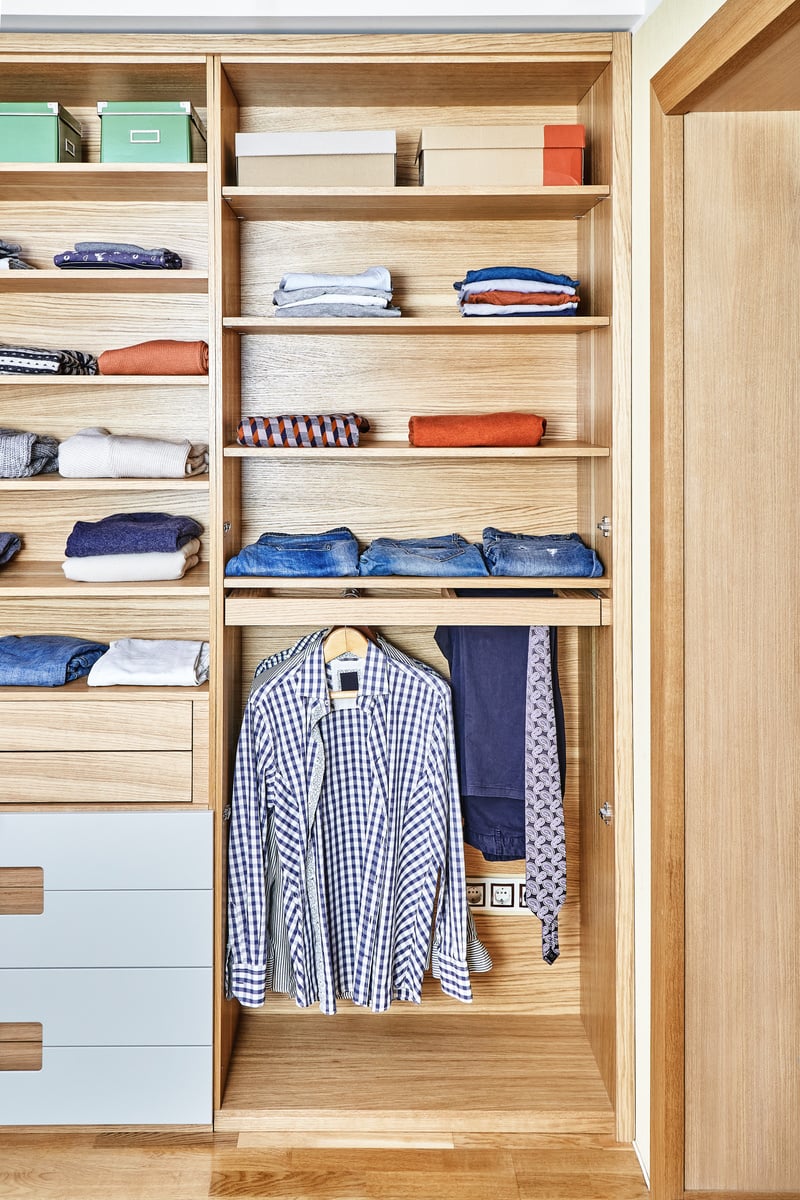 Modern wardrobe with clothes hanging on slide out racks and folded on the shelves. Modern furniture